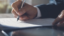 Person signing a document with a pen in their right hand